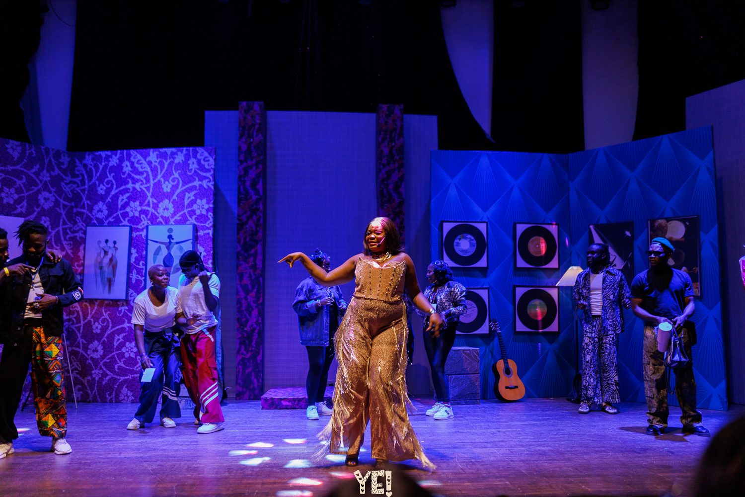 A performer in a gold fringed jumpsuit leads the YE! company