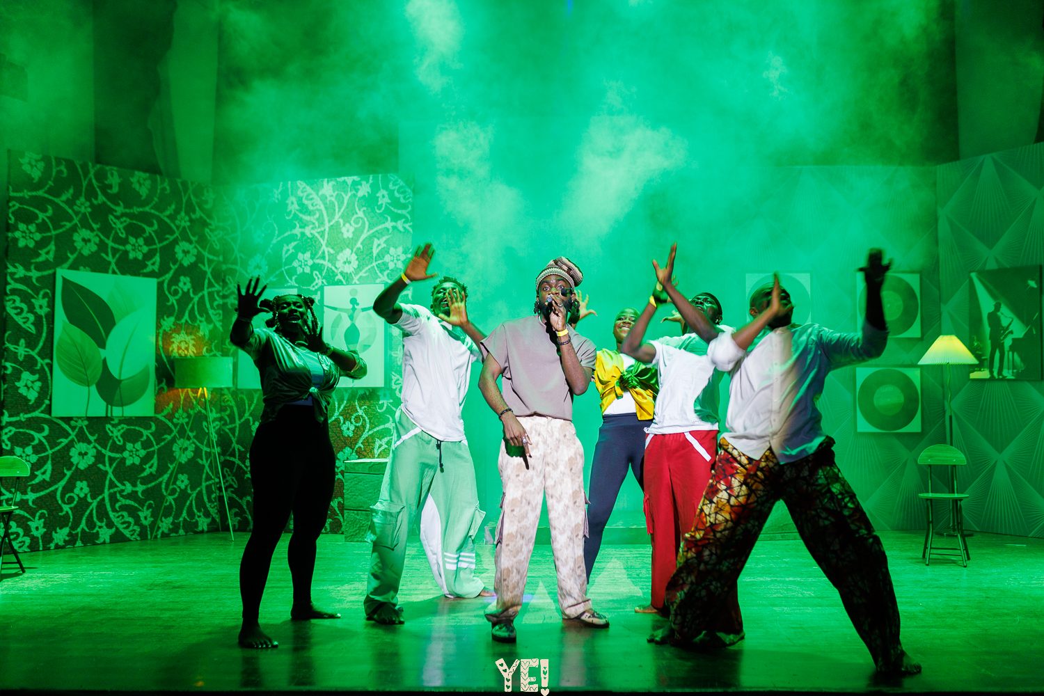 A YE! lead raps into the mic with dancers behind him in green light