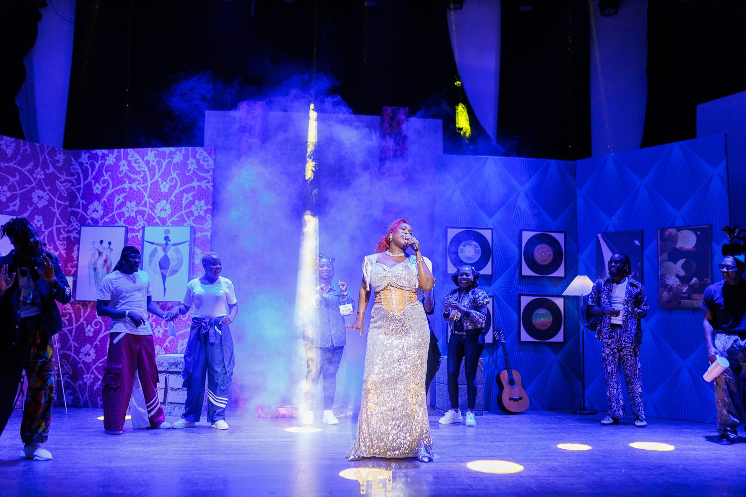 A singer in a silver gown performs under a blue spotlight in YE!
