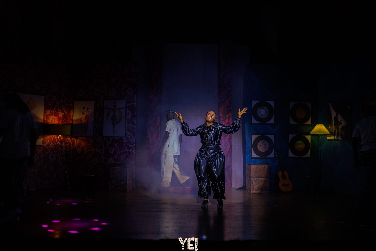 A YE! performer steps into a single spotlight on a dark stage