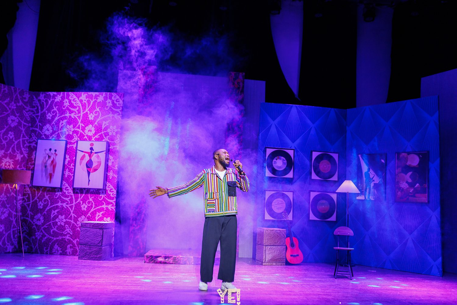 A YE! singer in a striped jacket performs through purple haze